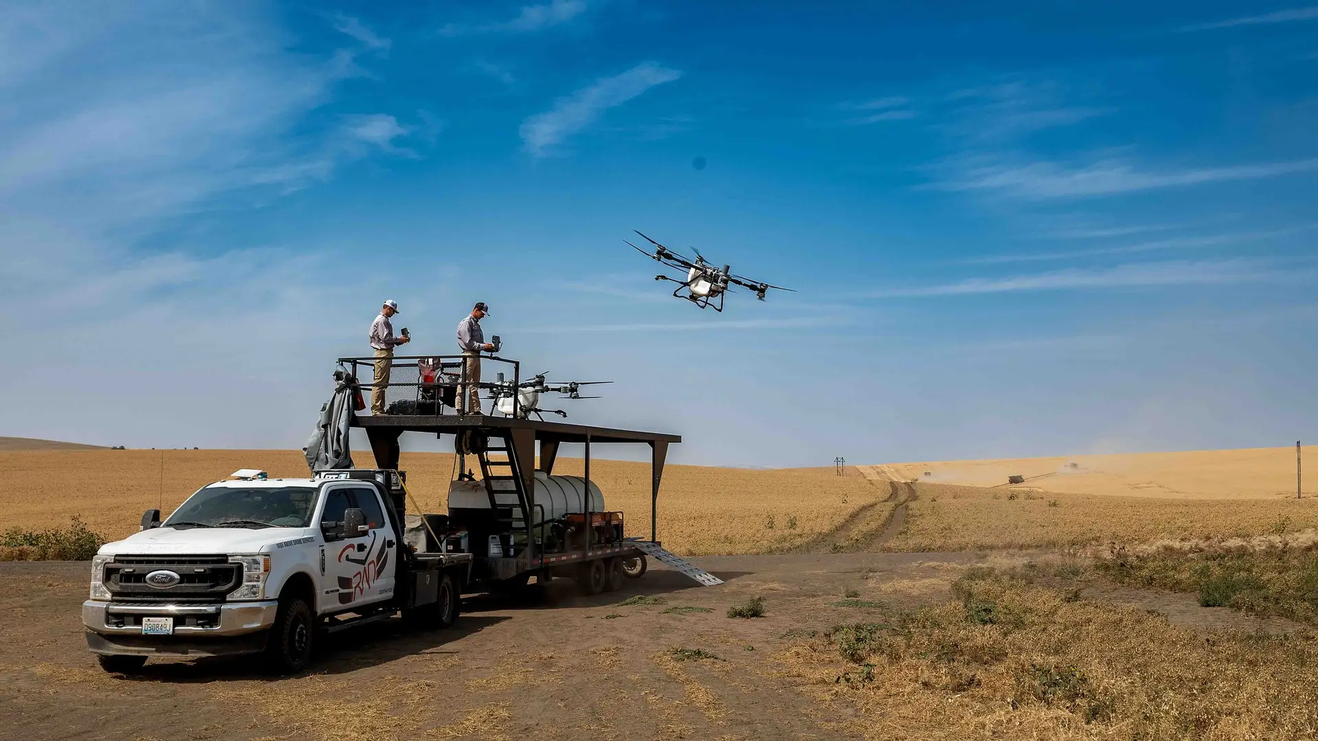 A RADS crew flies a DJI Agras spray drone from a truck-mounted platform at the edge of a harvested field