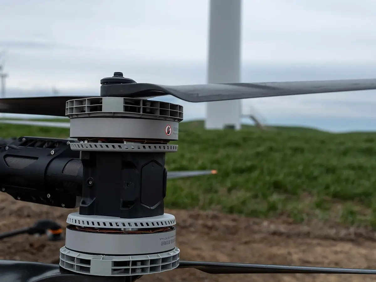 Close view of an Agras motor, propeller hub and arm with a wind turbine in the background