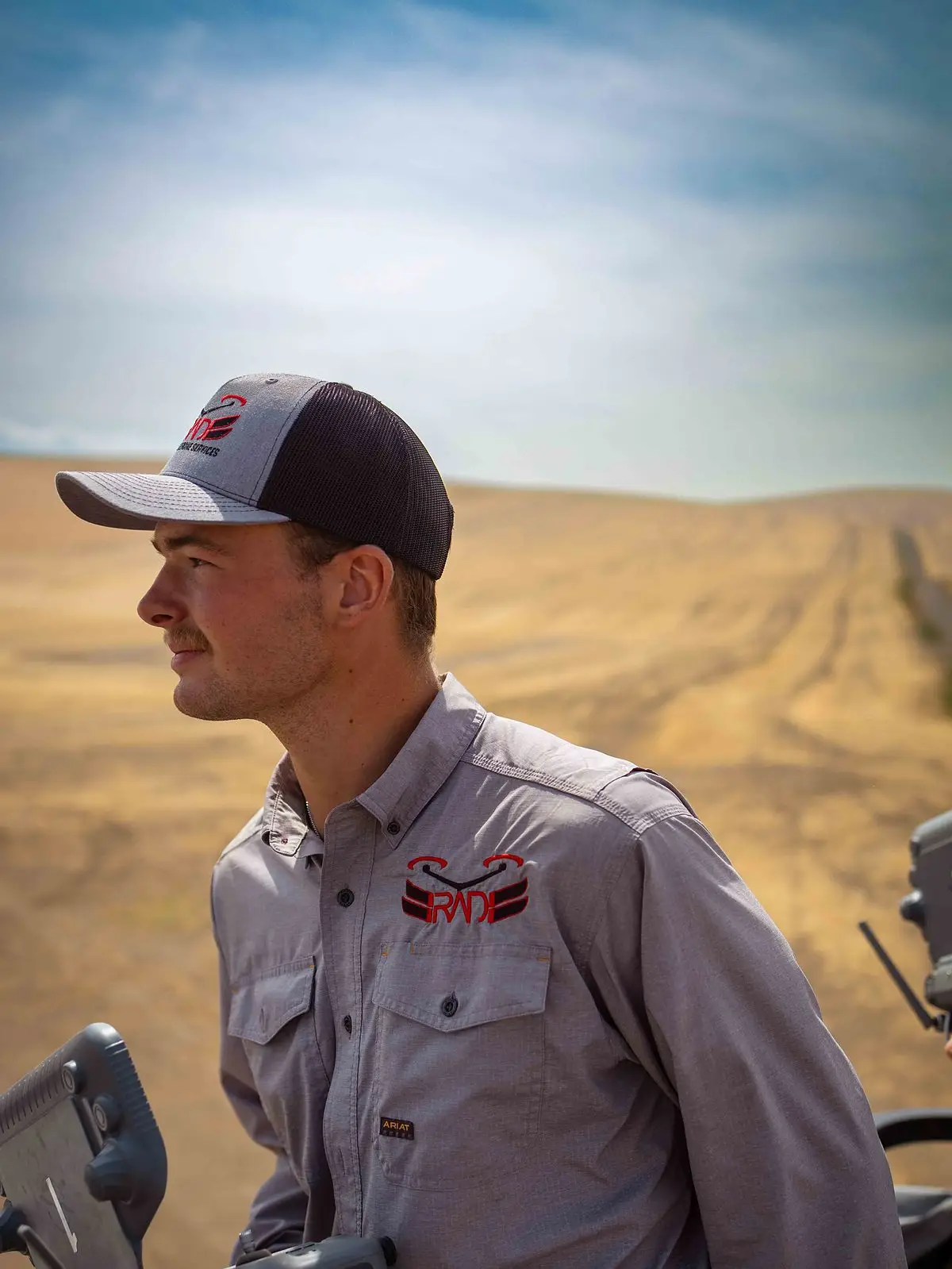 A RADS pilot in a company cap holds a DJI remote controller and watches the field from the platform