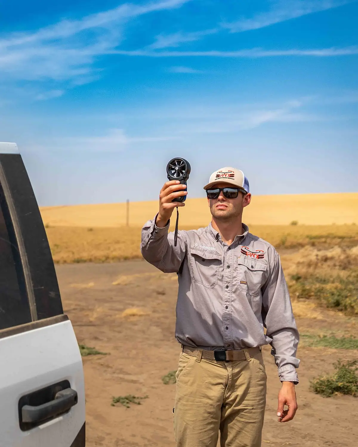A RADS operator checks wind speed with a handheld meter beside the service truck before an application
